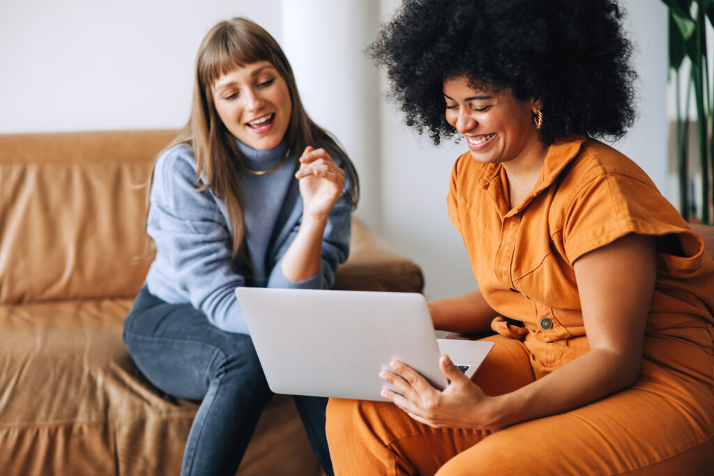 Two women smiling and looking at a real estate chat on a laptop screen together.