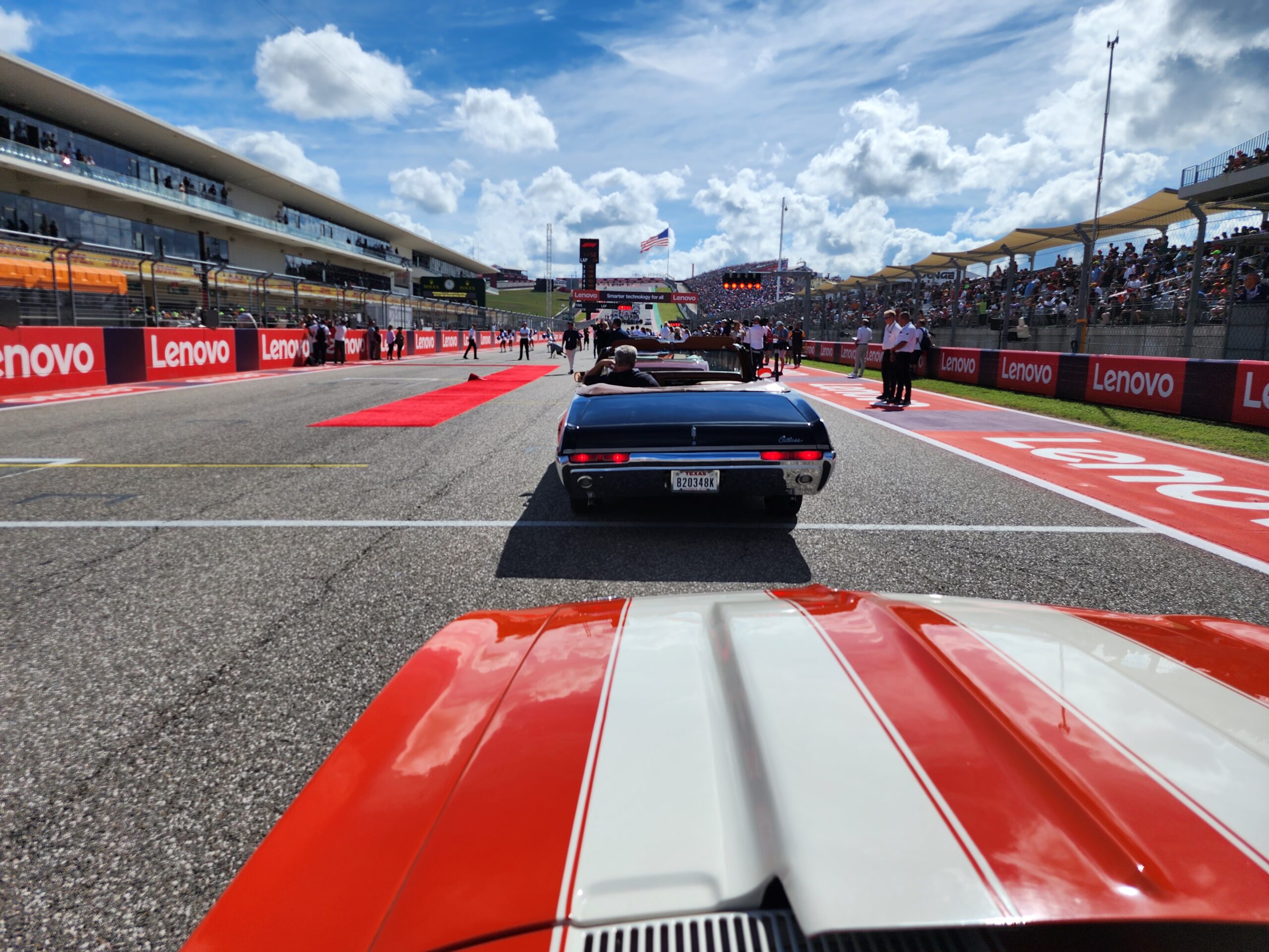 Classic car on a race track with spectators and racing crew in the background, highlighting the adventurous spirit sought after by Austin Realtor clients in home buying.