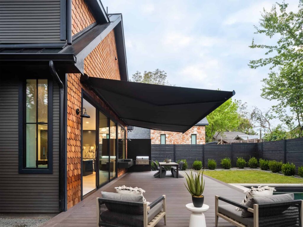 A modern backyard with a black awning and patio furniture perfect for relaxing or entertaining guests.