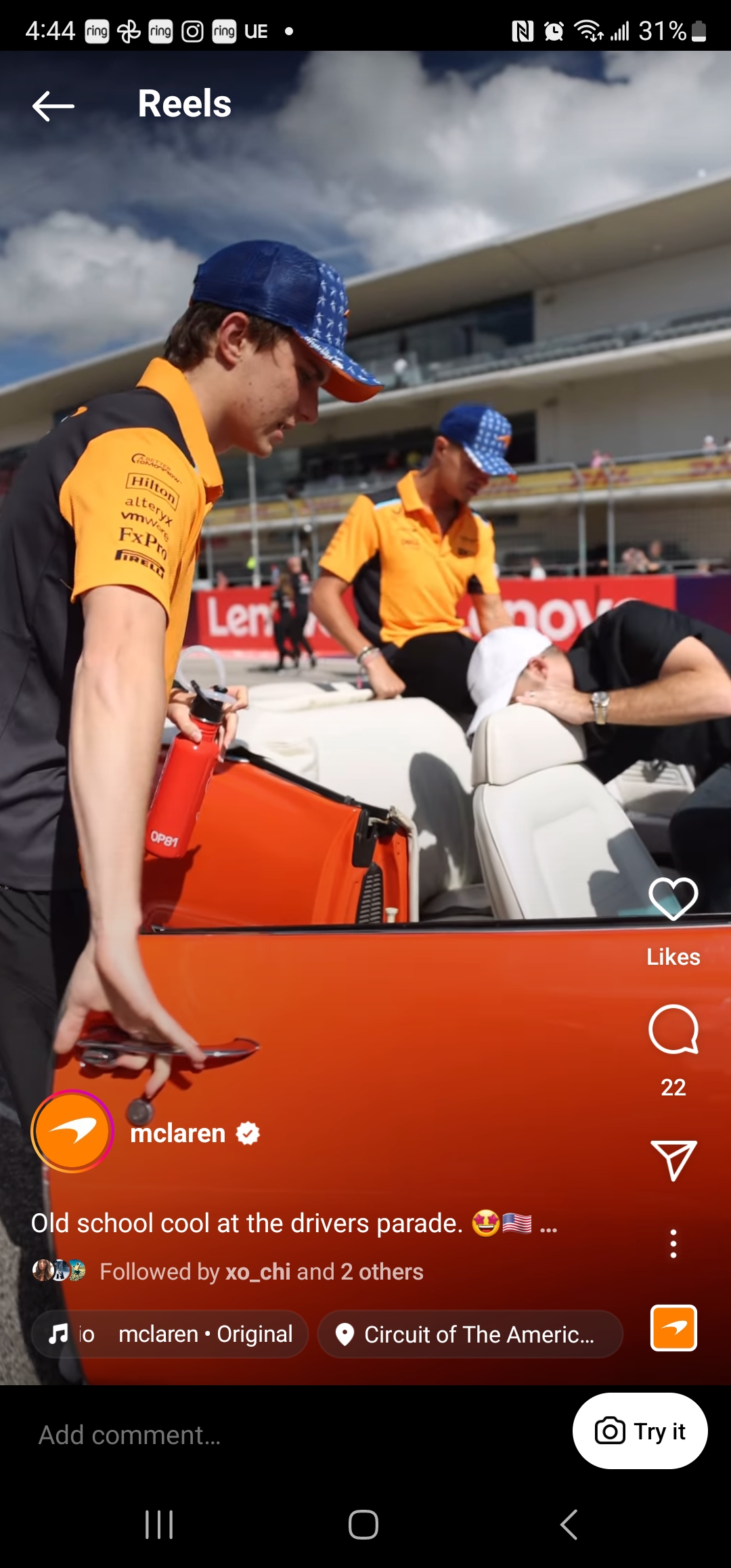A person in a McLaren racing team uniform adjusts a protective cover on a sports car during a home buying event parade.