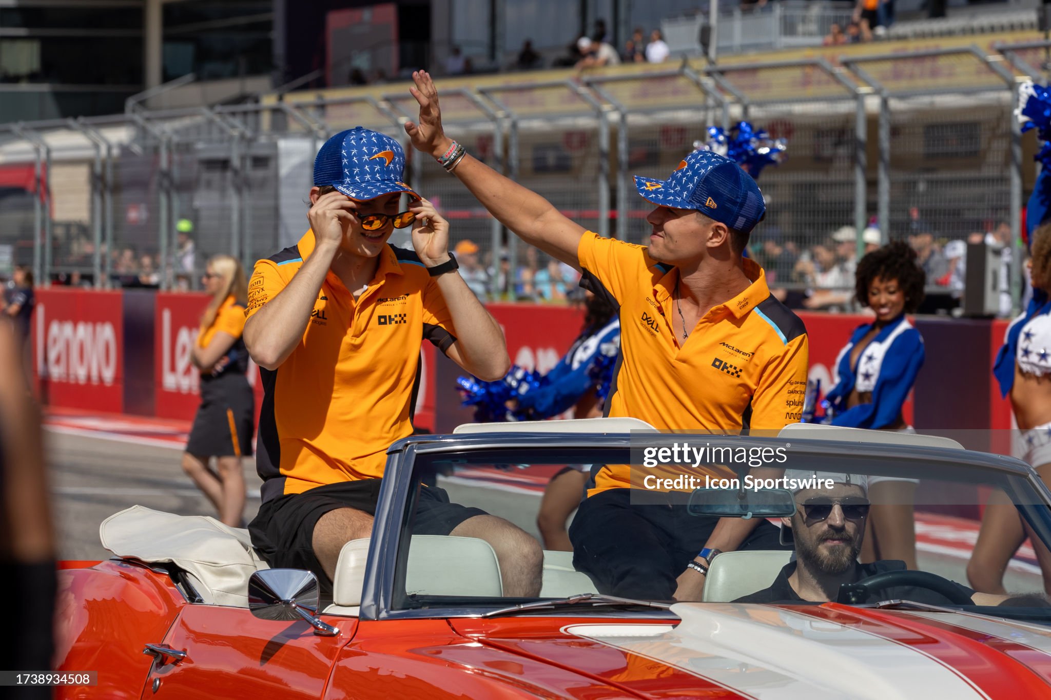 Two individuals wearing matching outfits and caps wave to a crowd from a convertible during a parade or event, discussing real estate chat.