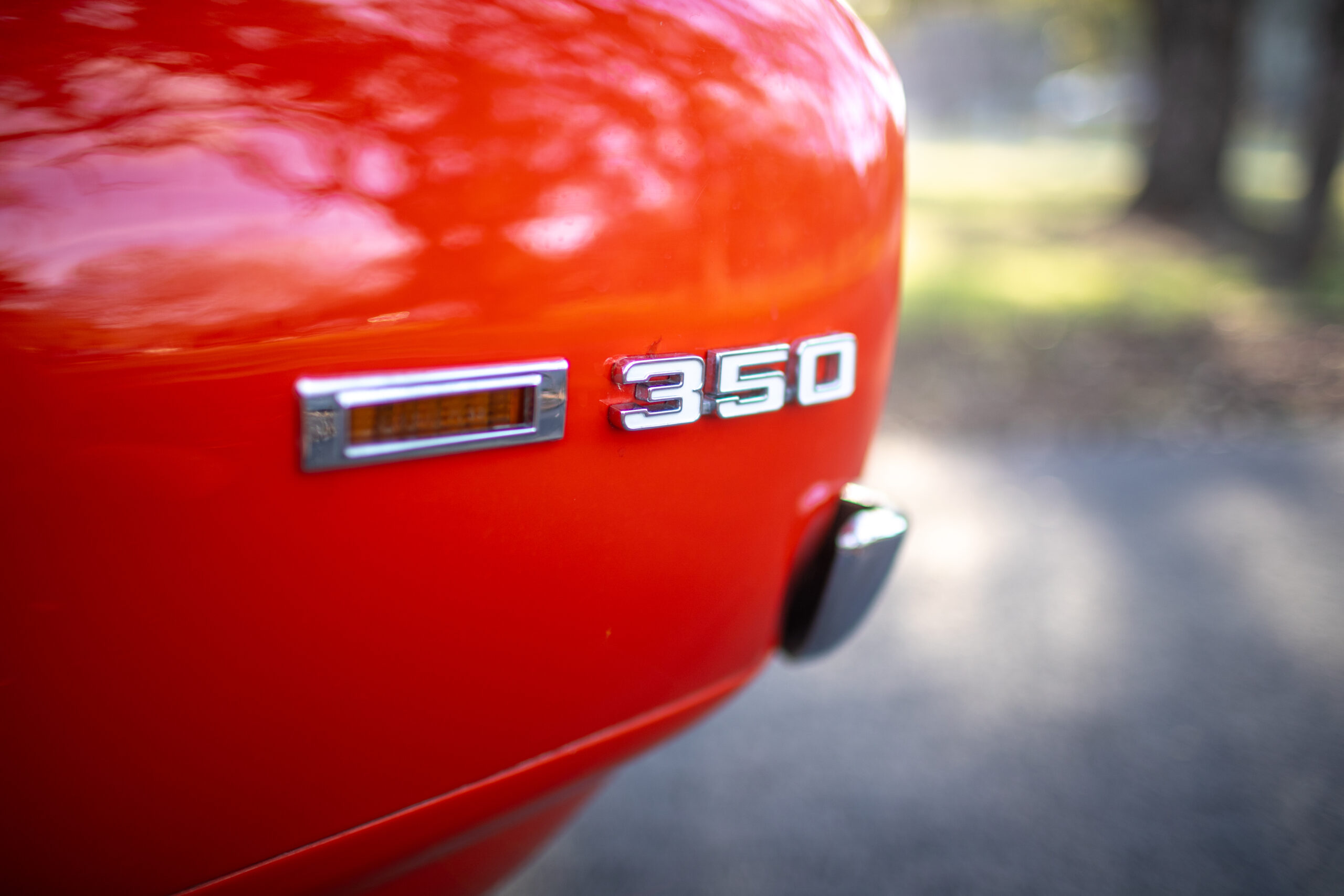 Close-up view of a red car rear bumper displaying a chrome "350" badge and a rectangular side marker light.
