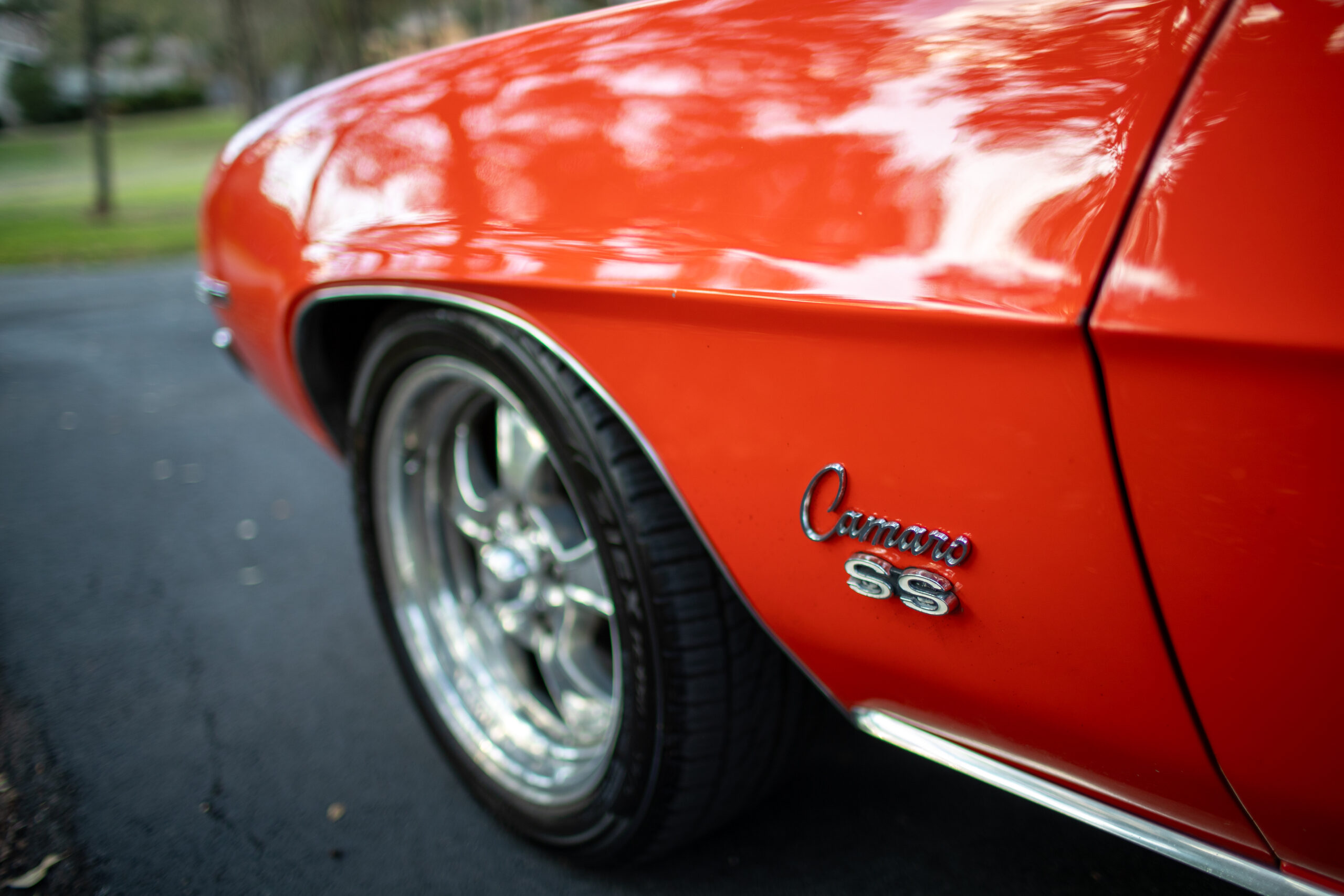 Close-up view of a red Chevrolet Camaro SS parked on a pavement, showcasing the "Camaro SS" emblem and a portion of the car's wheel.