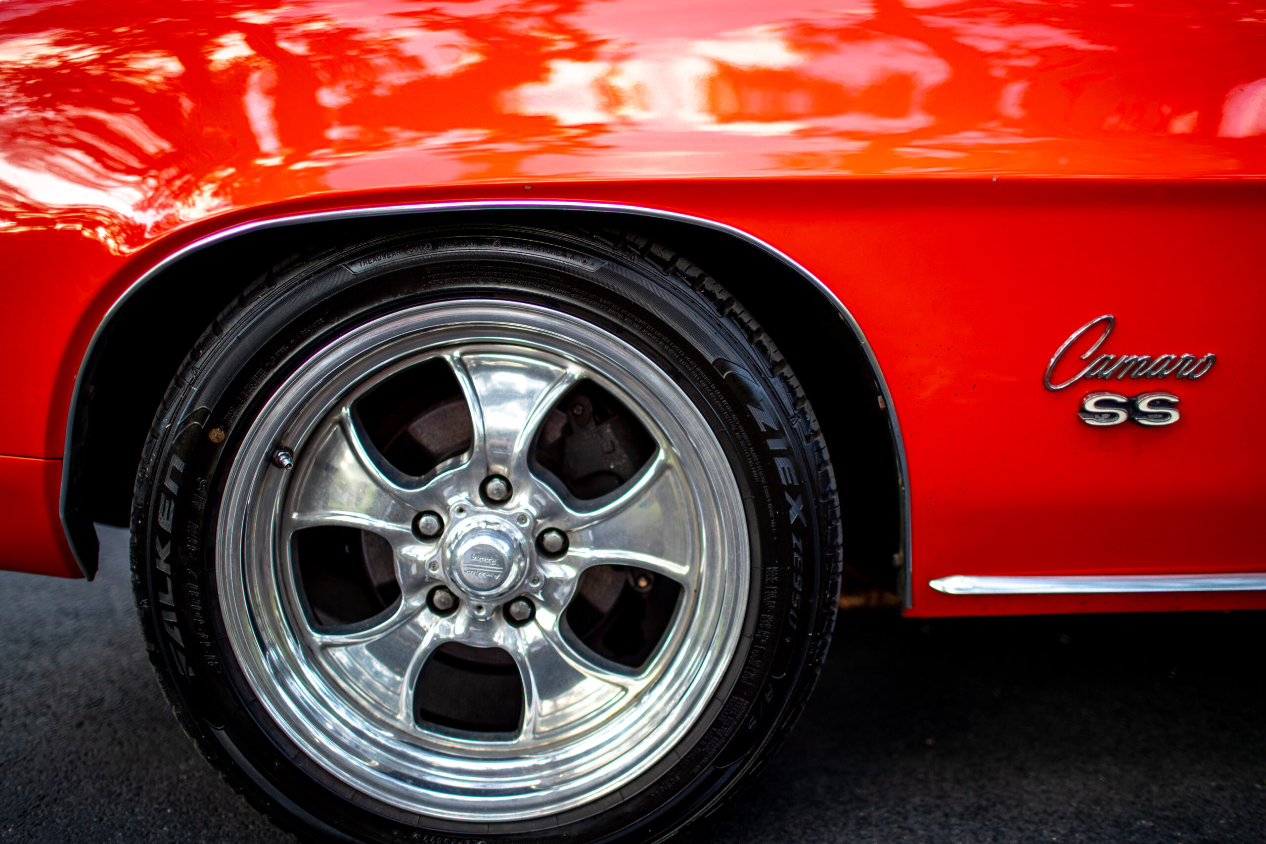 Close-up of a red sports car's wheel and fender, featuring a shiny chrome wheel and "Camaro SS" badge on the side.