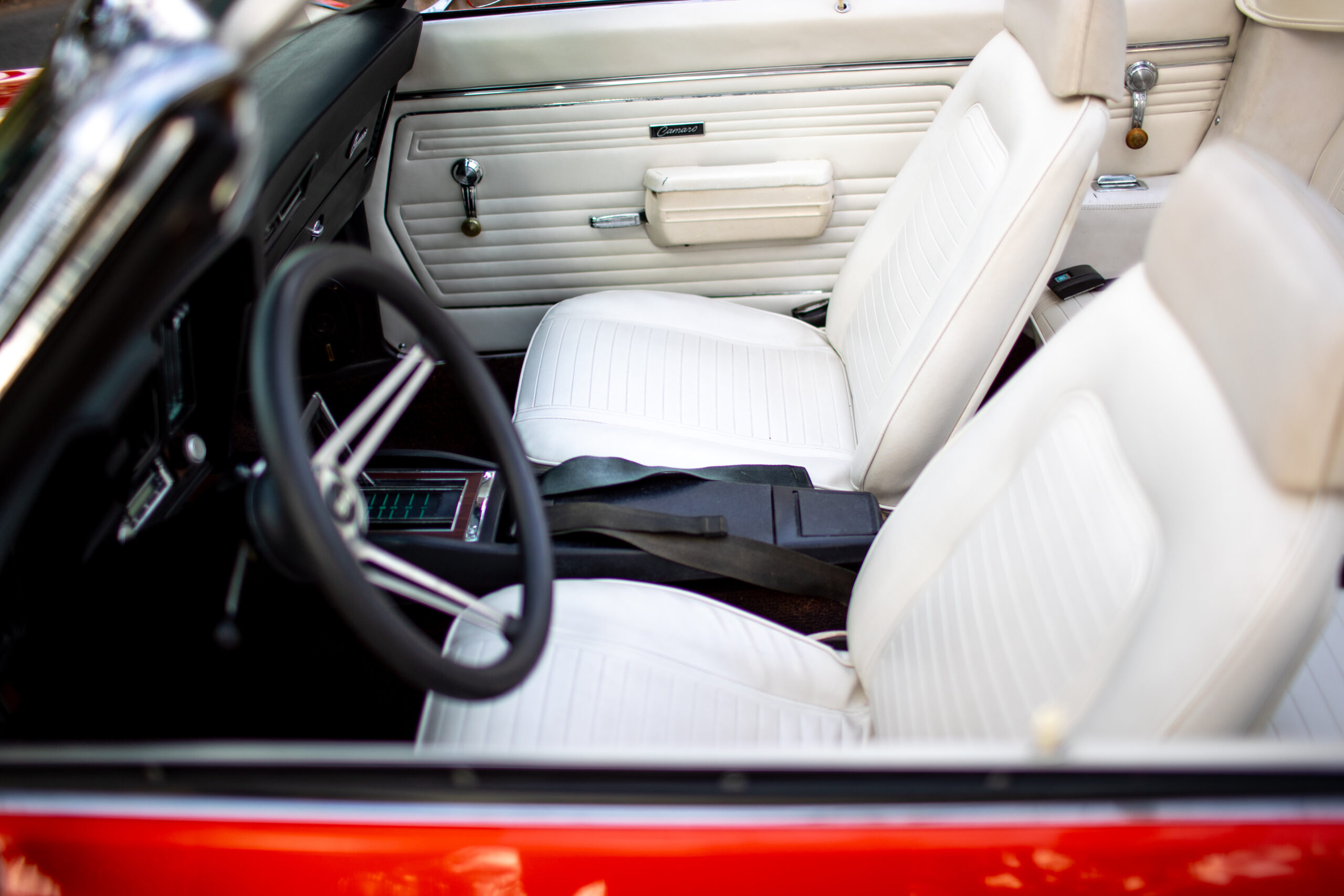 Interior view of a vintage red convertible car with white leather seats, black steering wheel, and door panel components.