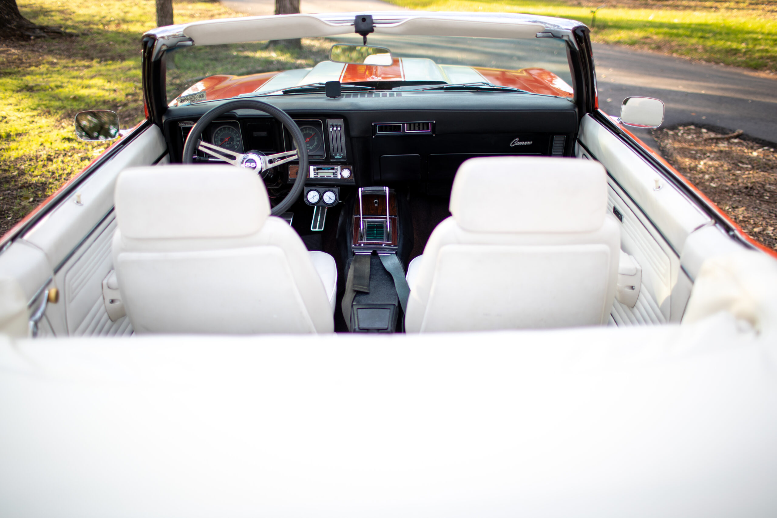 Interior view of a vintage convertible car with white seats, a black dashboard, and red exterior. The top is down and the car is parked outdoors on a sunny day.