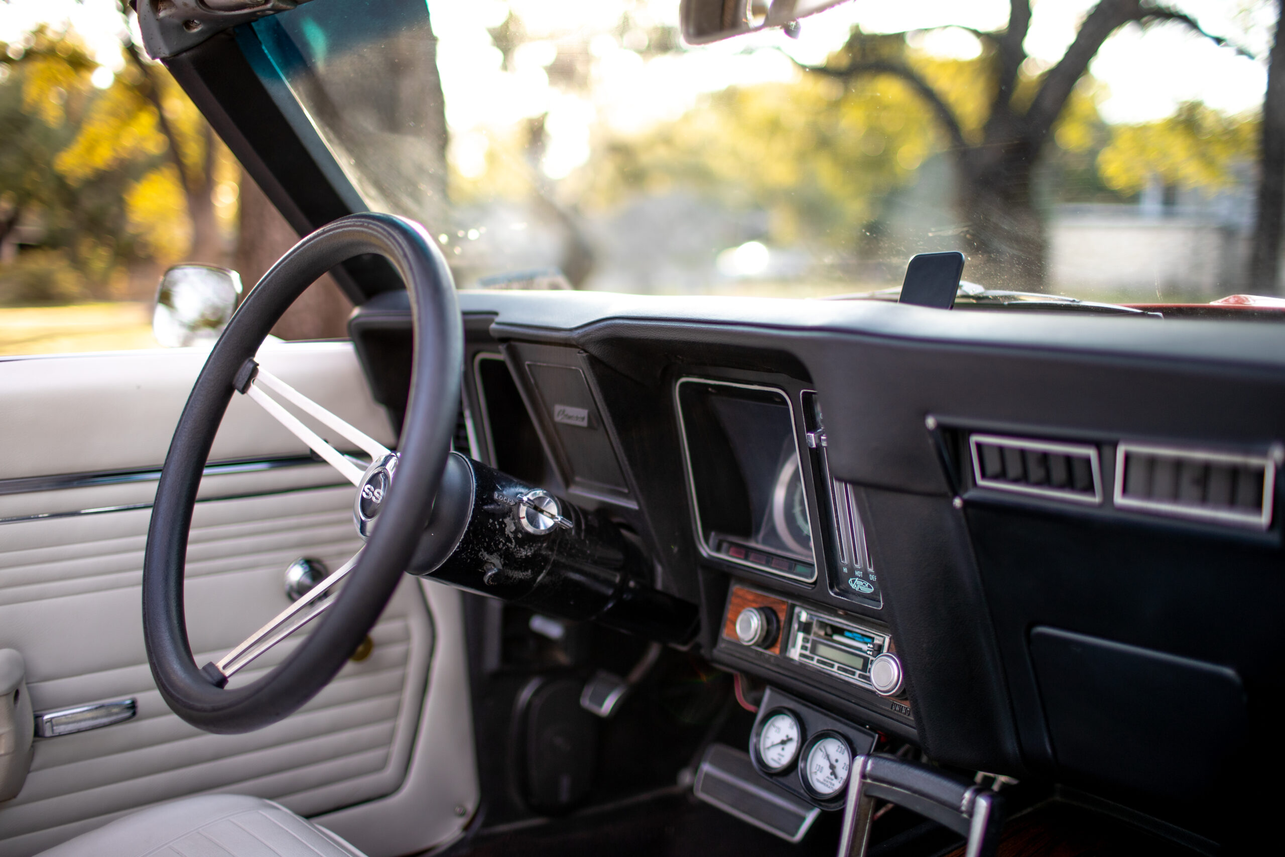 Interior view of a classic car focusing on the steering wheel, dashboard, and vintage radio controls with outdoor scenery visible through the windows.
