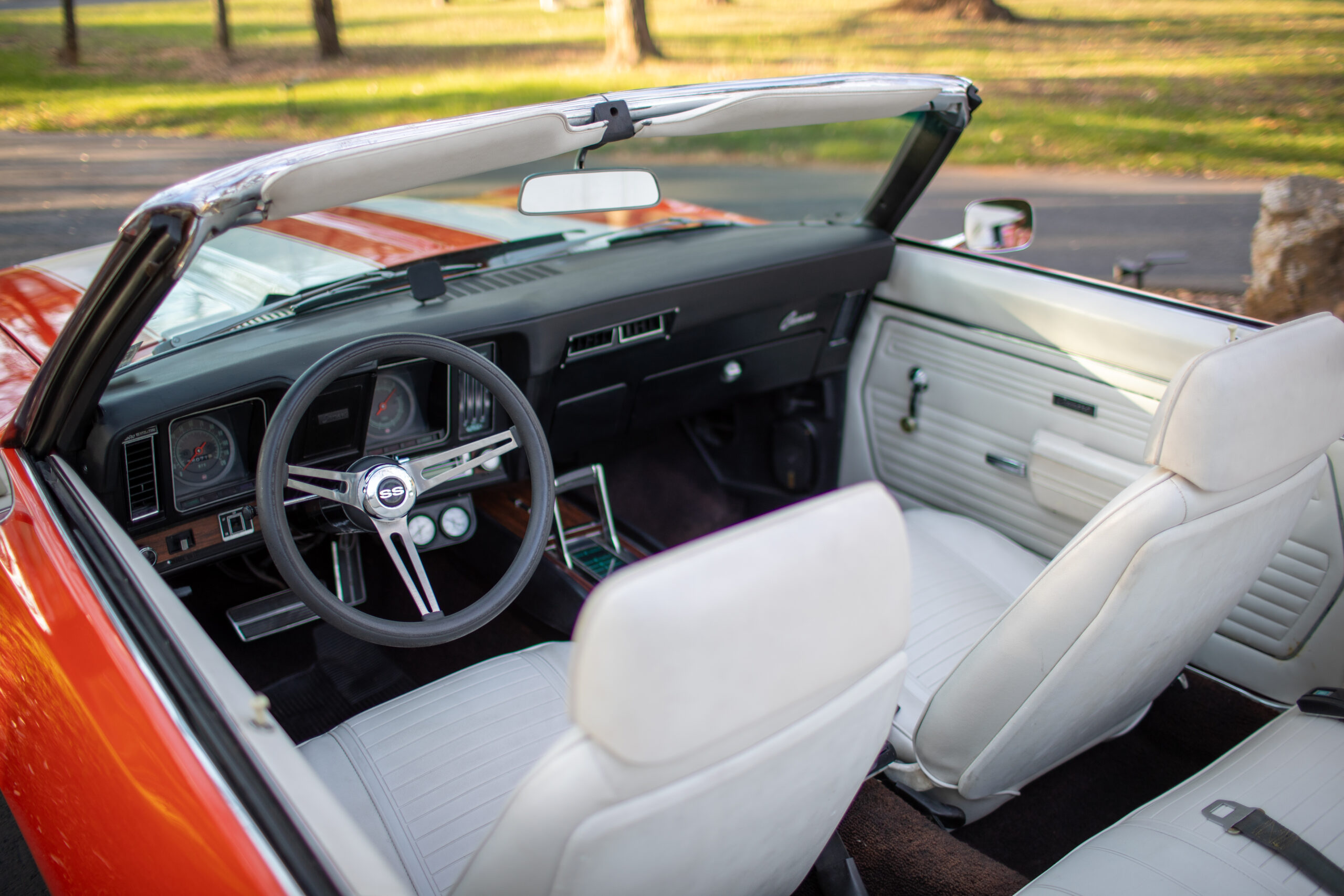 Interior view of a vintage convertible car with an orange exterior, white seats, and a classic steering wheel.