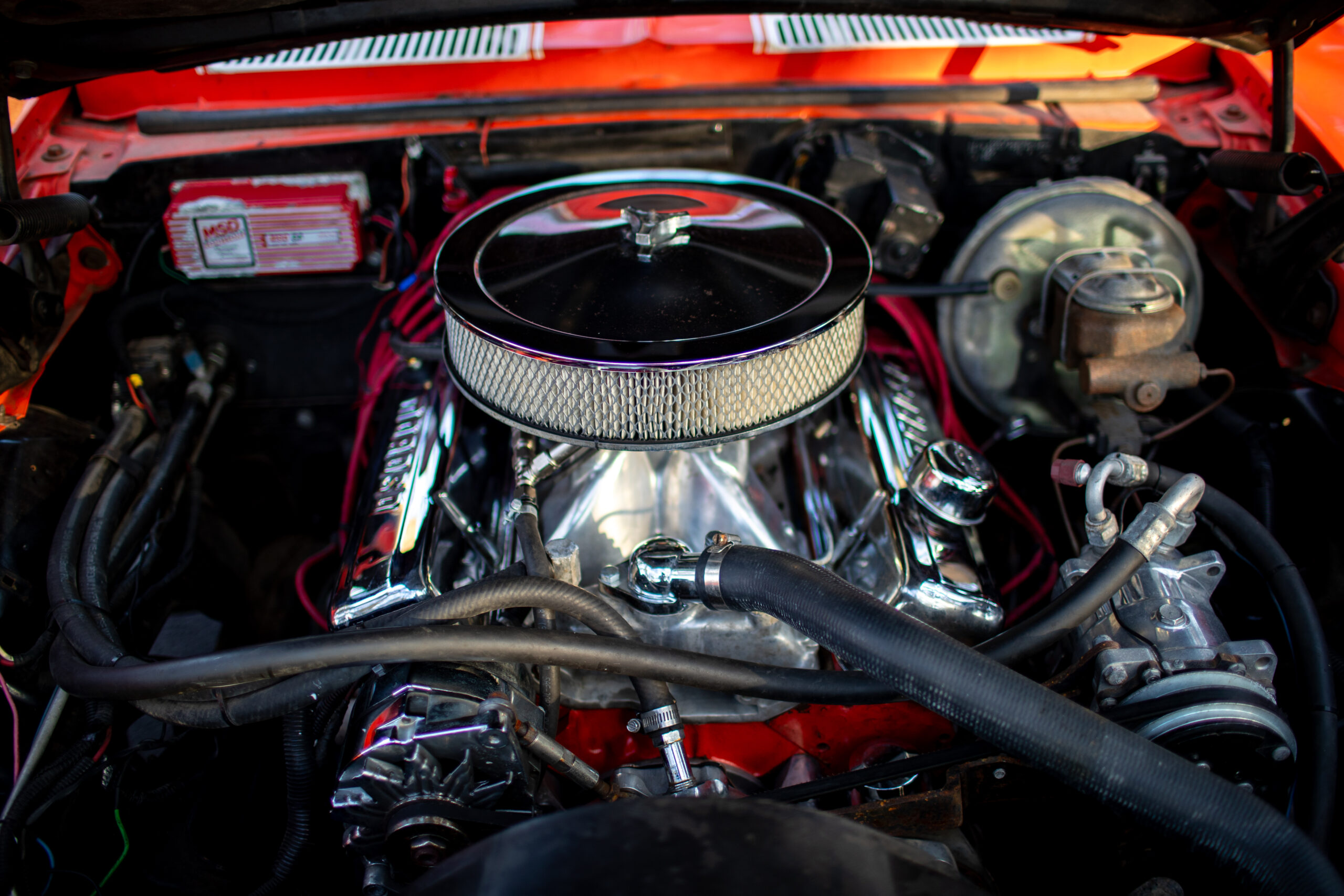 Close-up of a car engine with a chrome air filter, various hoses, and components visible.