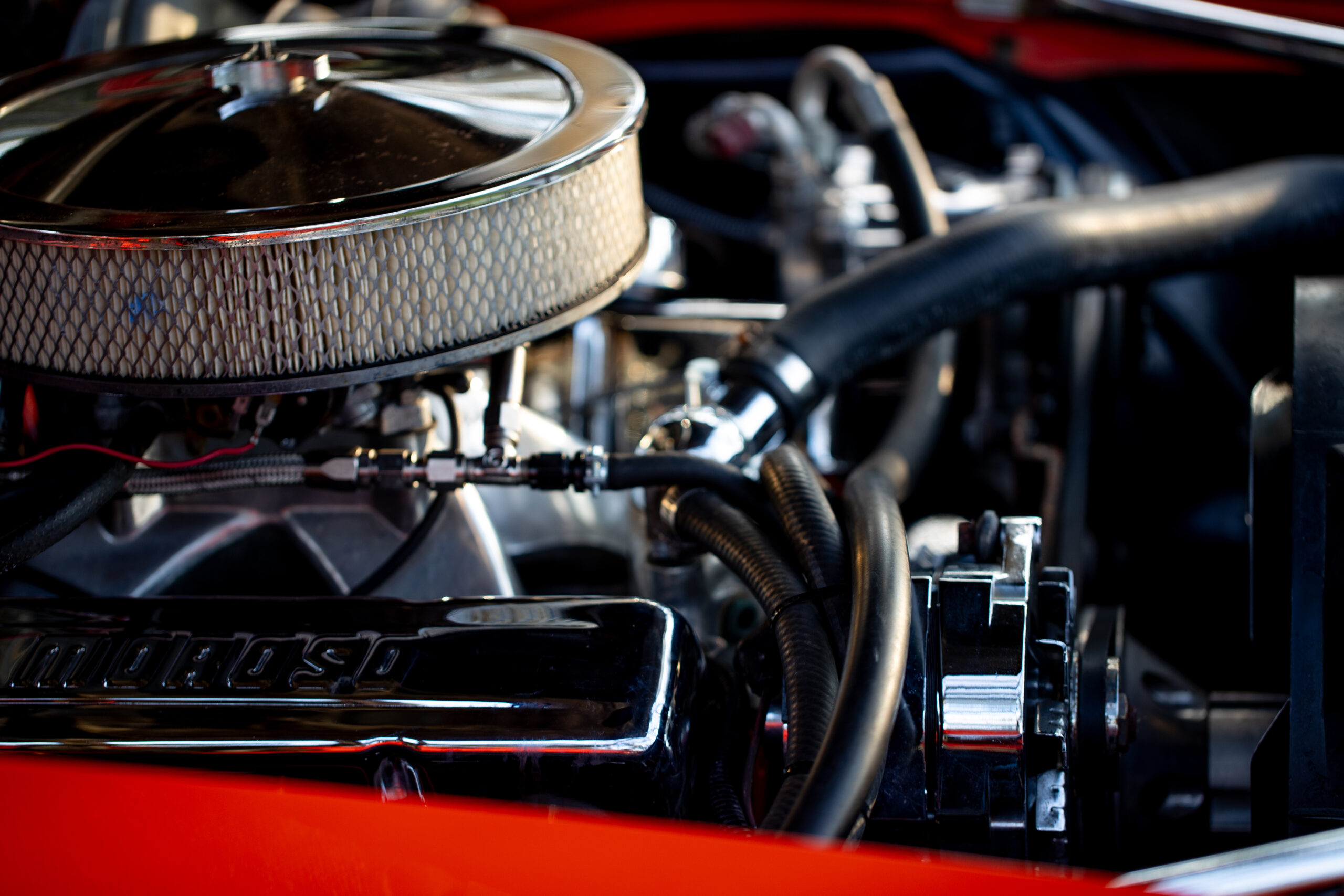 Close-up of a car engine showing polished components, black hoses, and a large circular air filter in a metal housing.