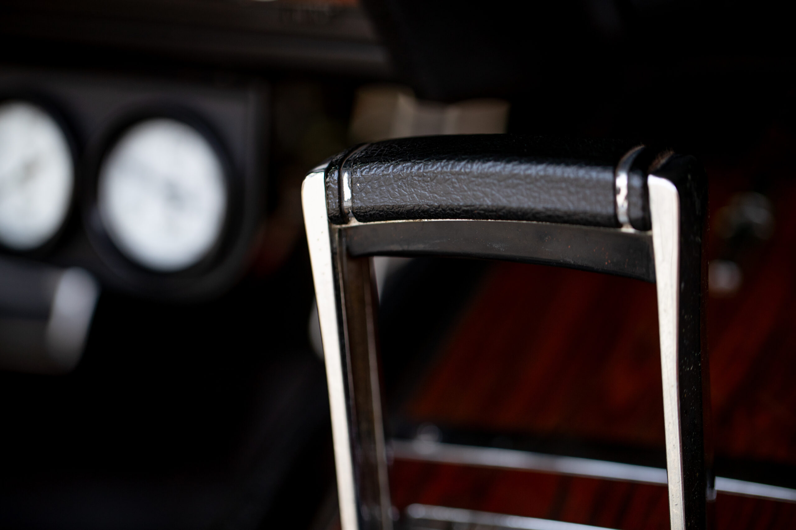 Close-up of a car's gear shifter with a leather handle, metallic accents, and part of the dashboard with gauges visible in the background.