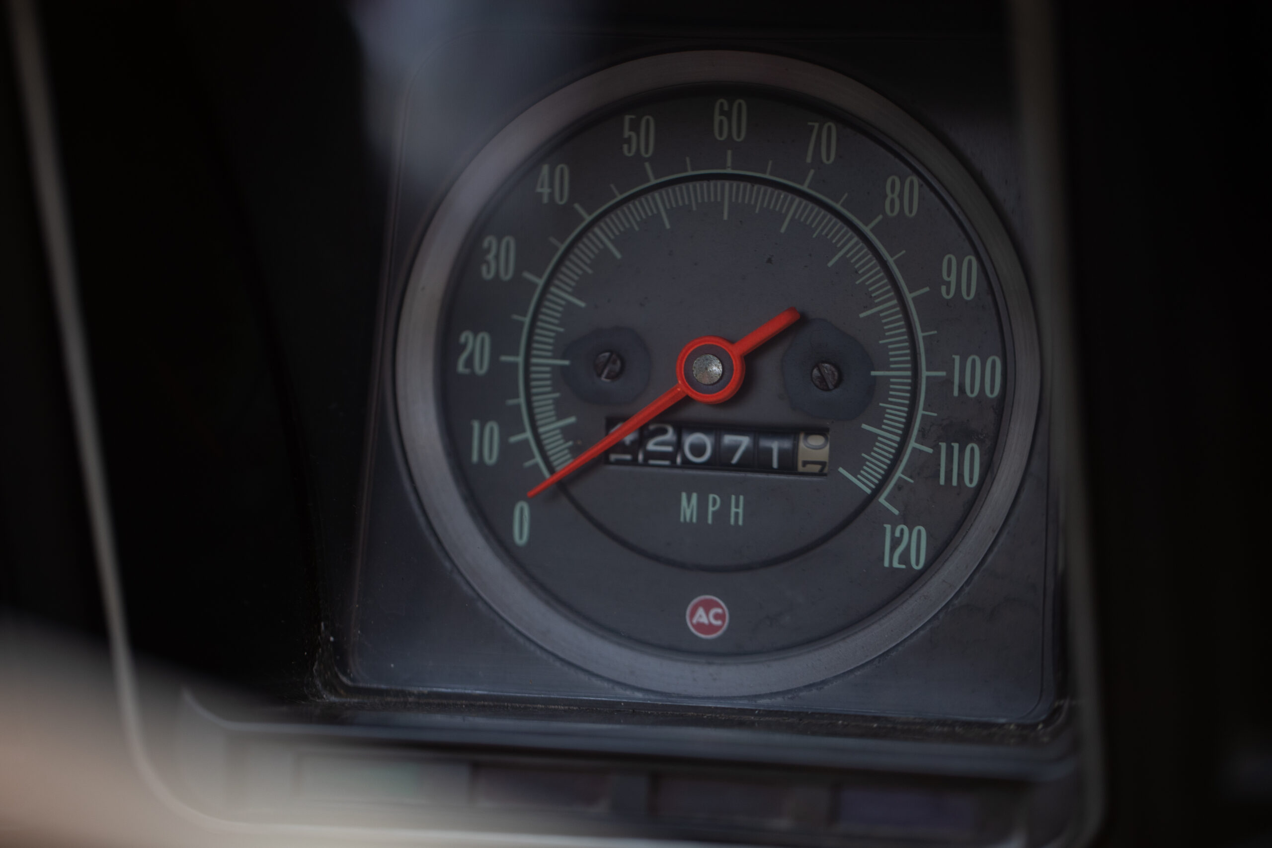 Close-up image of a car's analog speedometer showing a speed of 0 mph with an odometer reading of 12077 miles.