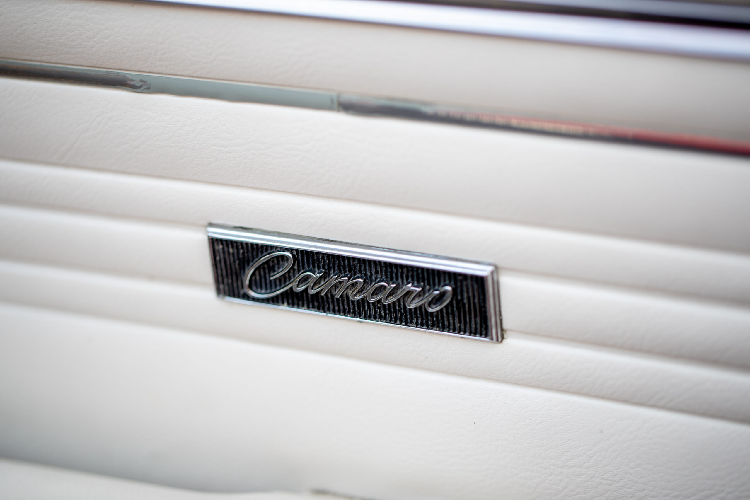 Close-up of a metal "Camaro" emblem on a white car door panel.