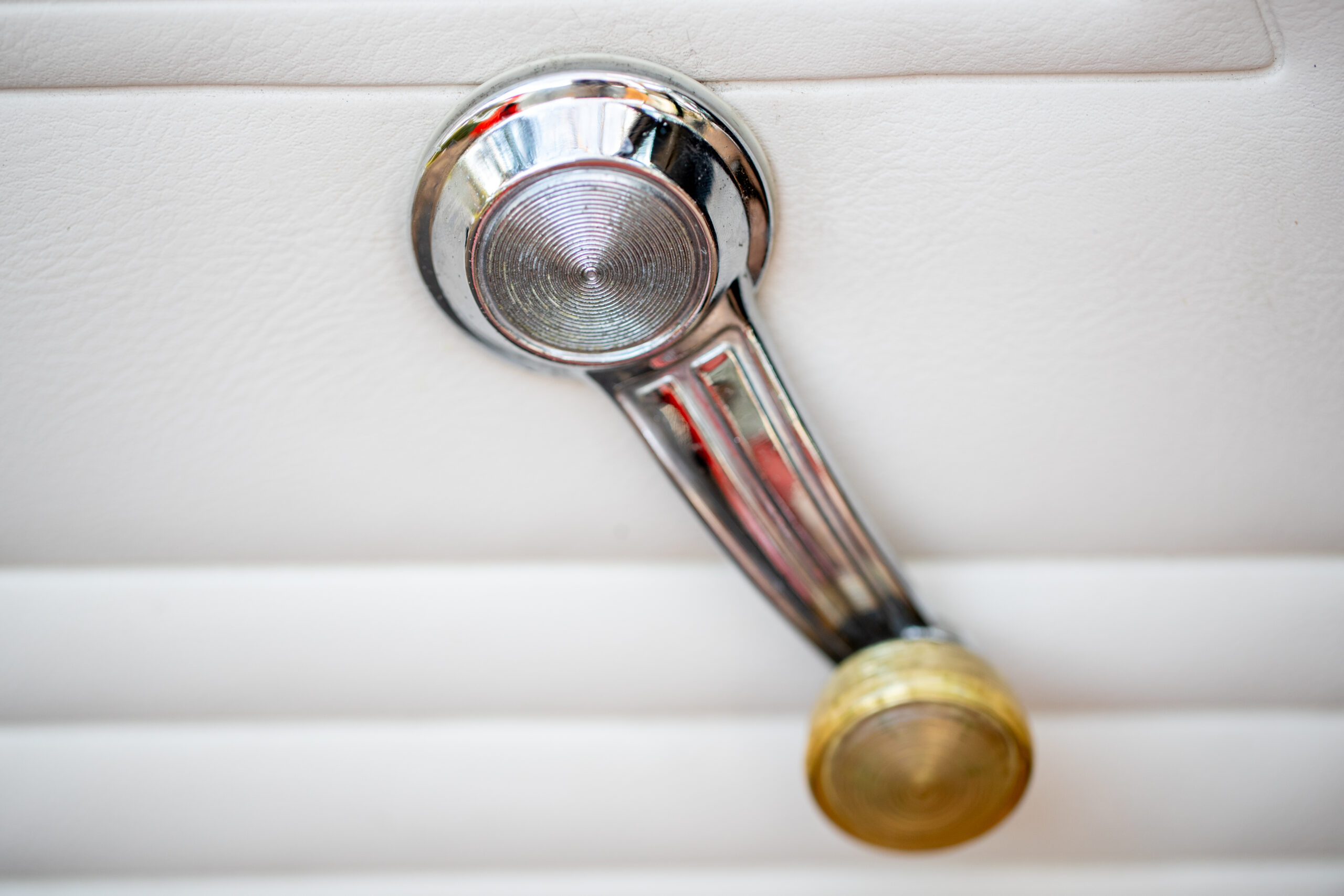 Manual window crank handle on a white car door panel.