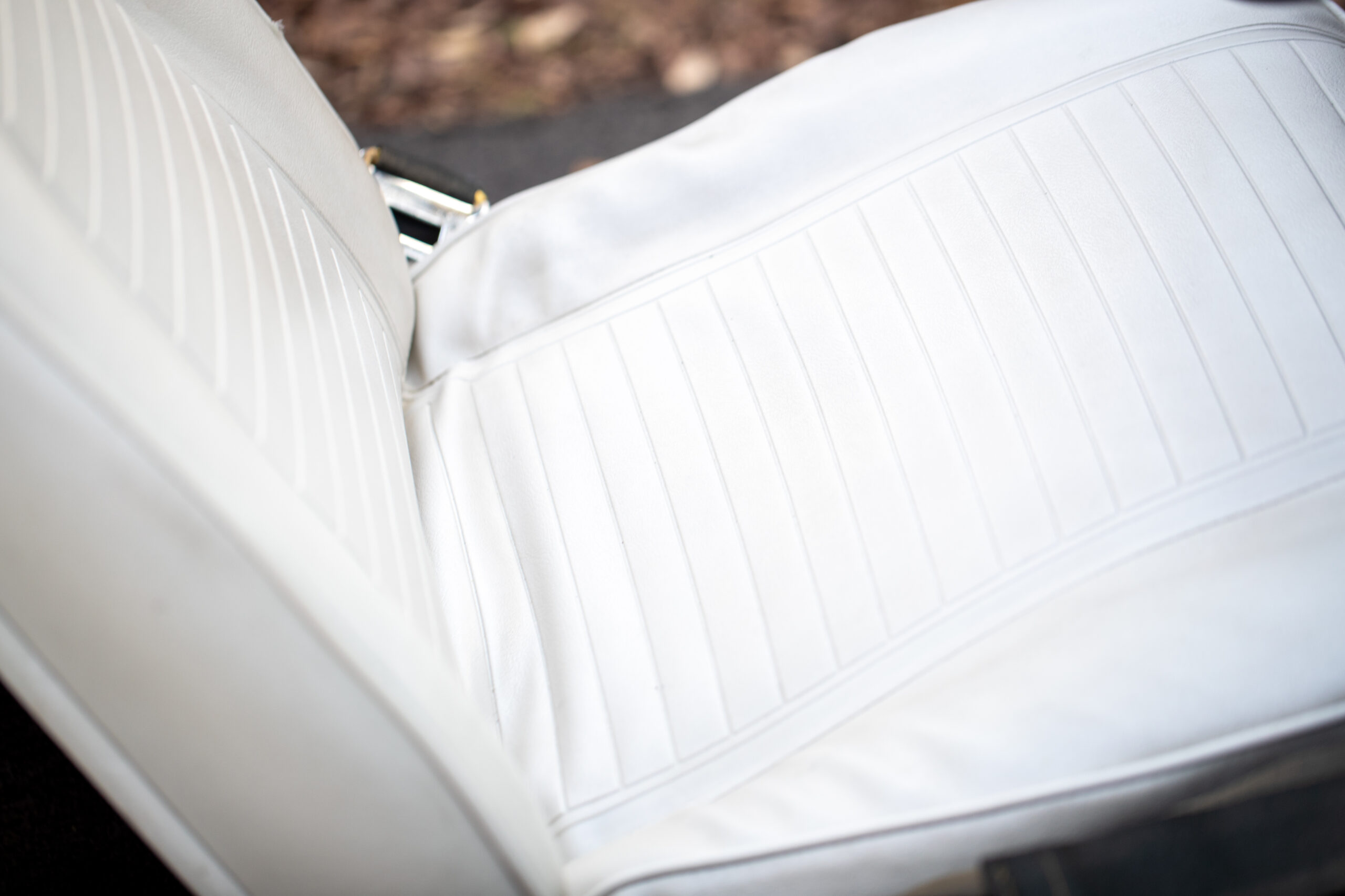 Close-up of a car's white leather seat with vertical stitching details. The background is slightly blurred.
