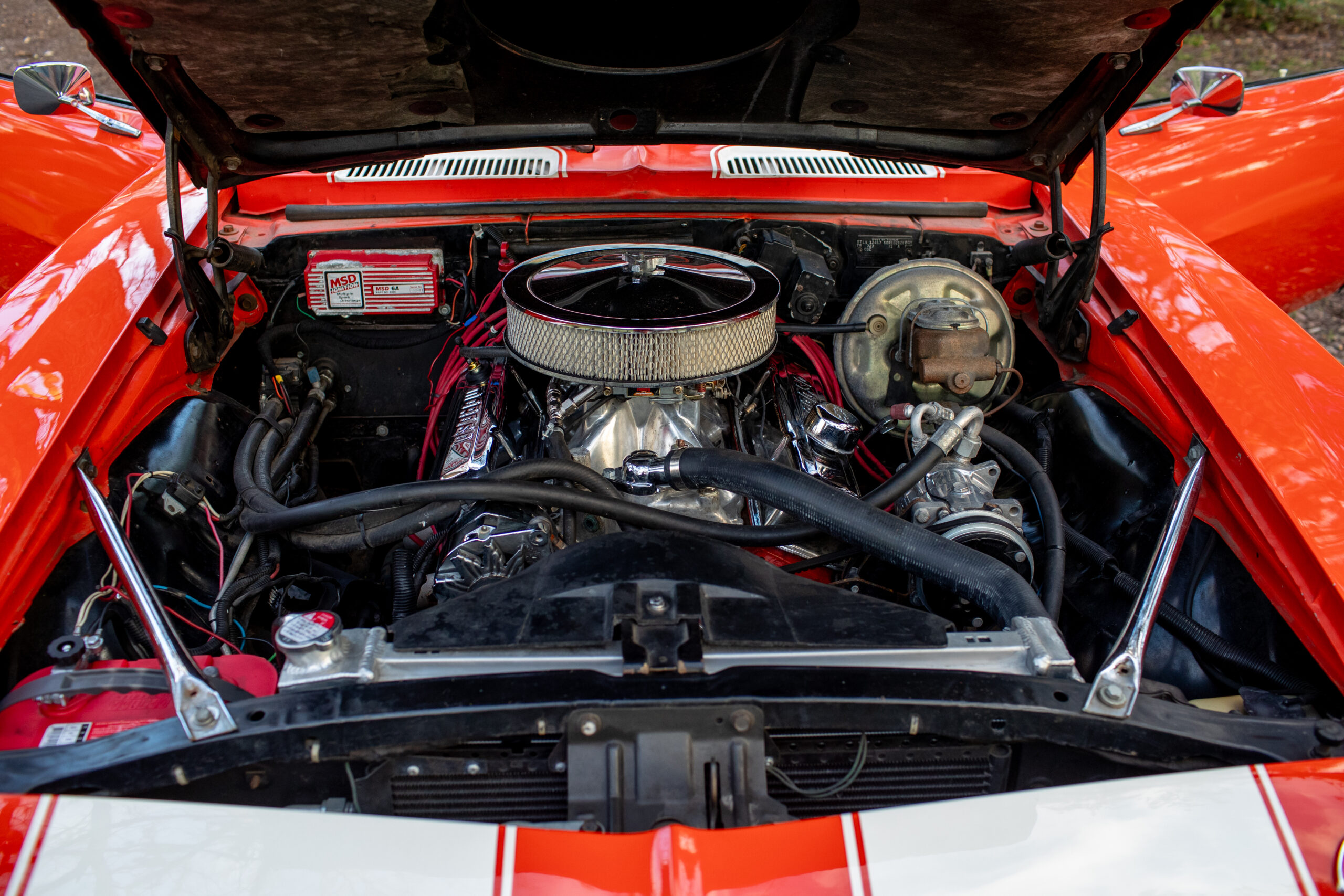 View of an open car hood revealing a clean, well-maintained engine with various components, wires, and a filter, in a red vehicle.